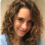 Image of Lauren Enders, a caucasian woman smiling at the camera. She has brown shoulder-length curly hair and is wearing a blue shirt.